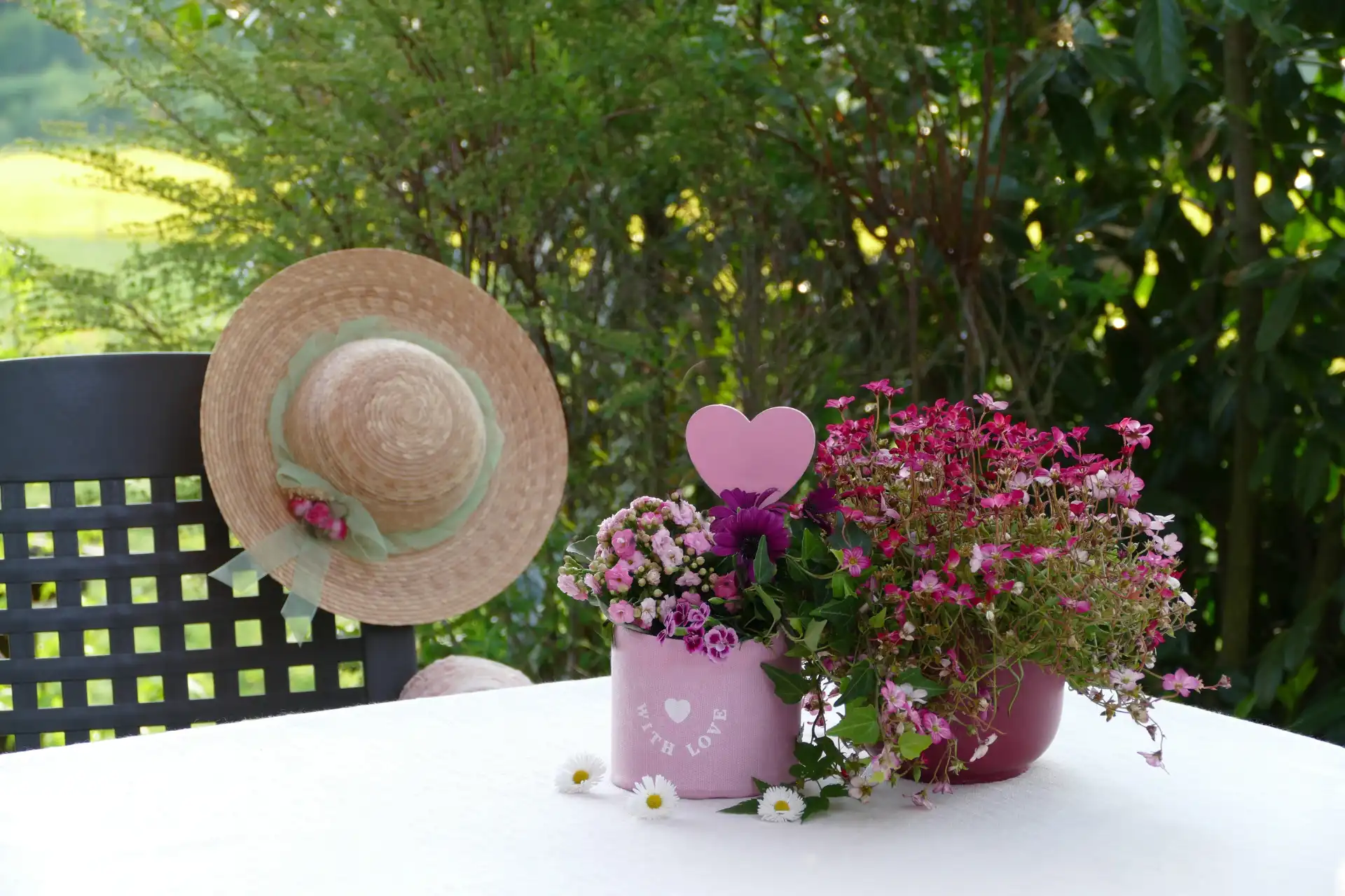 Still life of red and pink spring flowers with straw hat on table in garden